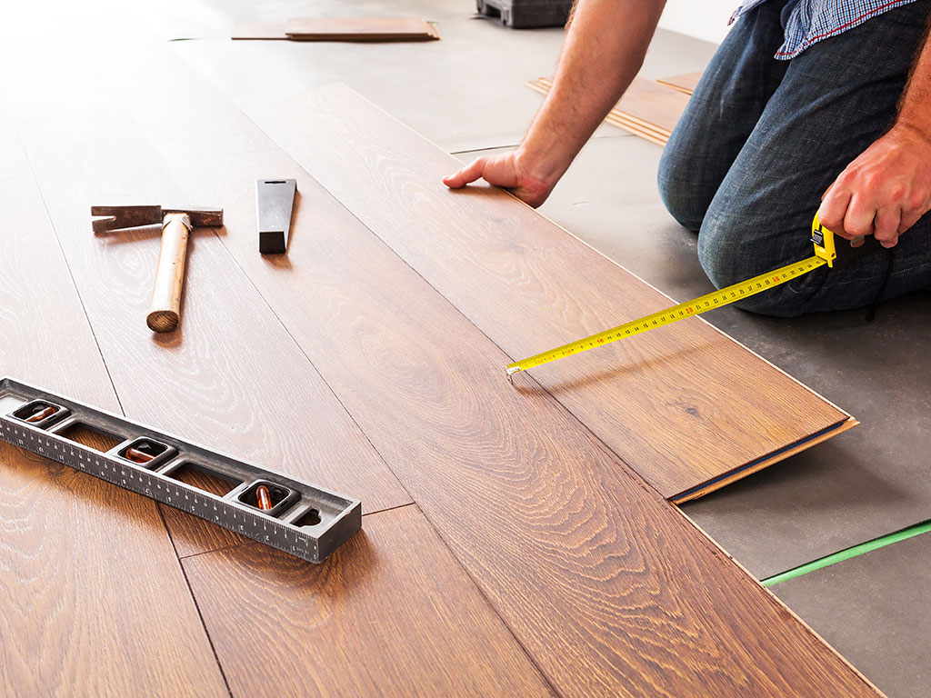 Worker measuring laminate floor with measuring tape and level