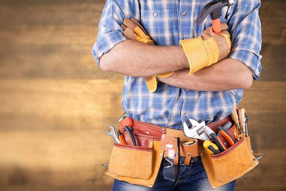 Man standing with tool belt full of tools in front of woodgrain background